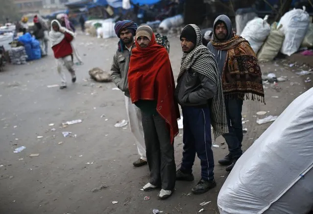 Men wearing shawls look on as they stand in a market place on a cold winter morning in the old quarters of Delhi December 31, 2014. (Photo by Ahmad Masood/Reuters)