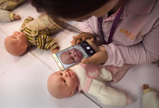 A Chinese woman takes a photo of a plastic baby used in a course as she and others train to be qualified nannies, known in China as ayis, at the Ayi University on October 28, 2016 in Beijing, China. The Ayi University training program teaches childcare, early education, housekeeping, and other domestic skills. The eight-day course costs US $250, and provides successful participants with a certificate to present to prospective employers. Most of the women attending the program are migrants from villages and cities across China who have moved to the capital to earn income to send home to their own families. China's burgeoning middle class has boosted demand for domestic help in urban areas, and the need for qualified childcare is expected to grow. In 2015, the government dismantled its controversial 'one child policy' as a means of rebalancing China's aging population in order to stave off a demographic crisis. Couples are now allowed to have two children, though the availability and cost of quality childcare is cited as an obstacle for many middle class parents who want larger families. (Photo by Kevin Frayer/Getty Images)