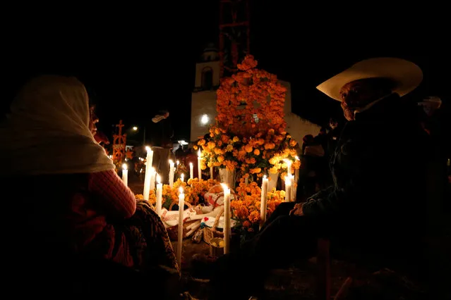 A couple sit next to the tomb of their loved one on the Day of the Dead at a cemetery in Arocutin, in Michoacan state, Mexico November 1, 2016. (Photo by Alan Ortega/Reuters)