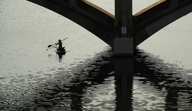 A woman glides along Lady Bird Lake on a paddle board in triple-digit heat in Austin, Texas, Wednesday, June 21, 2023. (Photo by Eric Gay/AP Photo)
