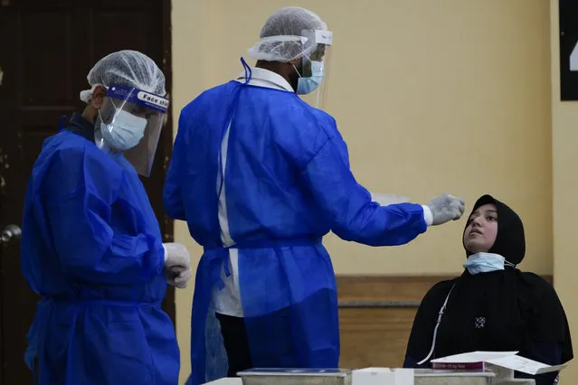 A medical worker collects a swab sample from a woman during coronavirus testing in Petaling Jaya, Malaysia, Monday, January 18, 2021. Malaysian authorities imposed tighter restrictions on movement to try to halt the spread of the coronavirus. (Photo by Vincent Thian/AP Photo)