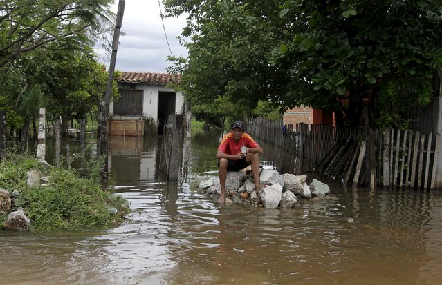 A man sits near houses are partially submerged in flood waters in Asuncion, December 20, 2015. (Photo by Jorge Adorno/Reuters)