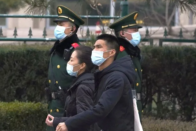 Residents wearing masks past by paramilitary officers on duty near the Great Hall of the People where delegates are attending the opening session of the Chinese People's Political Consultative Conference (CPPCC) held in Beijing on Thursday, March 4, 2021. (Photo by Ng Han Guan/AP Photo)