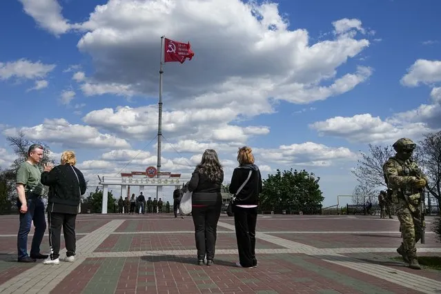 People look at a replica of the Victory banner fluttering in the wind over the central square in Melitopol, Zaporizhzhia region, in territory under Russian military control, southeastern Ukraine, May 1, 2022. Some in the West think Russian President Vladimir Putin may use the Victory Day on May 9 when Russia celebrates the defeat of Nazi Germany in World War II to officially declare that war is underway in Ukraine and announce a mobilization – the claim rejected by the Kremlin. (Photo by Alexander Zemlianichenko/AP Photo)
