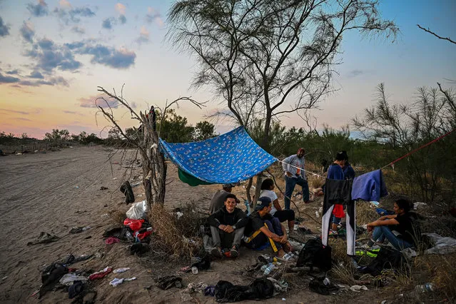Migrants rest after crossing the Rio Grande River as they wait to get apprehended by Border Patrol agents as National Guard agents sit on a car across the street (out of frame), in Eagle Pass, Texas, at the border with Mexico on June 30, 2022. Every year, tens of thousands of migrants fleeing violence or poverty in Central and South America attempt to cross the border into the United States in pursuit of the American dream. Many never make it. On June 27, around 53 migrants were found dead in and around a truck abandoned in sweltering heat near the Texas city of San Antonio, in one of the worst disasters on the illegal migrant trail. (Photo by Chandan Khanna/AFP Photo)