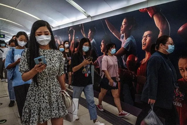 Commuters wear protective masks as they walk by a billboard showing some of China's Olympic athletes in the subway on August 6, 2021 in Beijing, China. While cases still remain relatively low compared to many countries, China is battling its worst COVID-19 outbreak in months after workers in the arrivals area at Nanjing International Airport were infected with the highly contagious Delta variant and it has since spread to dozens of cities in at least 18 provinces. (Photo by Kevin Frayer/Getty Images)