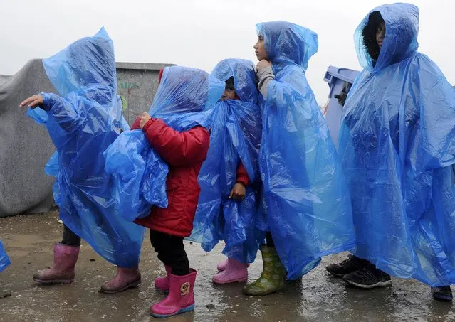 Children are covered with a plastic raincoat under heavy rainfall in a makeshift camp for refugees and migrants at the Greek-Macedonian border near the village of Idomeni, Greece, March 23, 2016. (Photo by Alexandros Avramidis/Reuters)