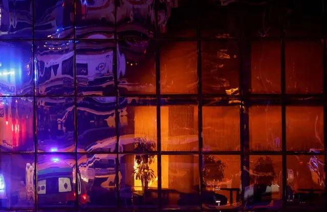 Ambulances are reflected in windows of the burning Crocus City Hall concert venue following a shooting incident, outside Moscow, Russia, on March 22, 2024. (Photo by Maxim Shemetov/Reuters)