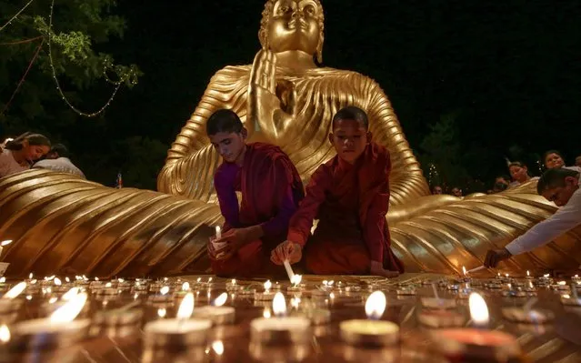 Young Buddhist monks light candles at the bottom of a giant statue of Buddha on the eve of Buddha Purnima, a holiday traditionnally celebrated for Buddha's birthday also known as Vesak celebrations, in Bhopal on 17 May, 2019. Buddhists are preparing to celebrate Vesak, which commemorates the birth of Buddha, his attaining enlightenment and his passing away on the full moon day of May which falls on May 18 this year. (Photo by Gagan Nayar/AFP Photo)