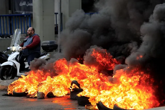 A man rides his scooter past burning tires at one of main roads during a protest against the increase in prices of consumer goods and the crash of the local currency, in Beirut, Lebanon, Monday, November 29, 2021. (Photo by Hussein Malla/AP Photo)