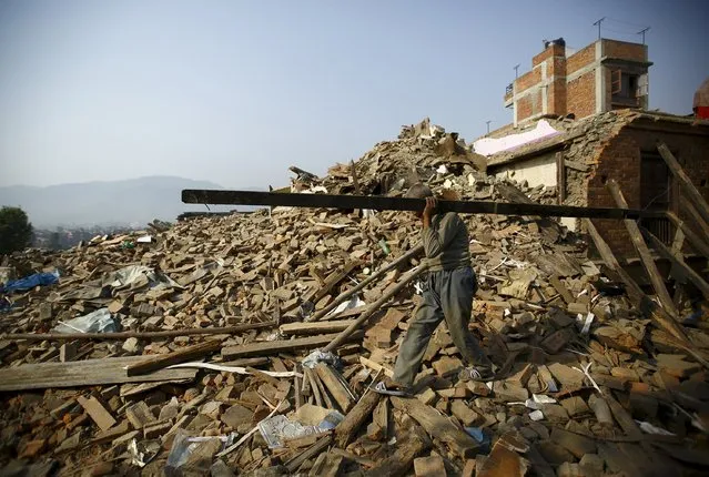 A man carrying a block of wood recovered from his house walks along the debris of collapsed houses, a month after the April 25 earthquake in Kathmandu, Nepal May 25, 2015. (Photo by Navesh Chitrakar/Reuters)