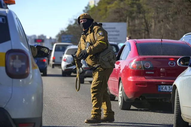 A member of the Ukrainian territorial defense directs cars in a traffic jam ahead of a military checkpoint outside Kyiv, Ukraine, Monday, February 28, 2022. (Photo by Vadim Ghirda/AP Photo)