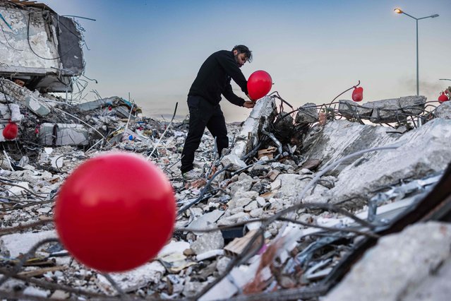 Ogun Sever Okur, 38-year-old Turkish man hangs a ballon on the debris of a collapsed building in Antakya, southern Turkey on February 21, 2023, following the 6.4-magnitude earthquake which struck on February 20, two weeks after a 7.8-magnitude earthquake hit near Gaziantep and has killed more than 44,000 people. On the side of a busy road in Antakya, dozens of red balloons flutter around, hanging from the ruins. They are “the last toys” of children who died during the earthquake that devastated this southern Turkish city, explains Ogun Sever Okur, the author of this posthumous gift. (Photo by Sameer Al-Doumy/AFP Photo)