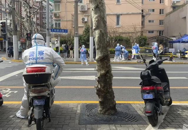 A police officer in protective gear watches over residents lining up for COVID tests in the Jingan district of western Shanghai, China, Friday, April 1, 2022. (Photo by Chen Si/AP Photo)