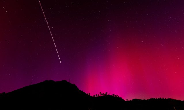 The blinking lights of a plane streak through the Aurora Borealis visible over Lake Berryessa, California on May 11, 2024. (Photo by Carlos Avila Gonzalez/AP Photo)