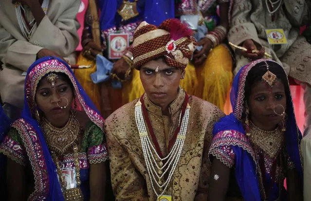 A groom sits next to brides as they pose for pictures during a mass wedding ceremony at Ramlila ground in New Delhi June 15, 2014. A total of 92 physically challenged couples of all religions from across India took their wedding vows on Sunday during the mass wedding ceremony organised by a non-governmental organisation (NGO), organisers said. (Photo by Adnan Abidi/Reuters)