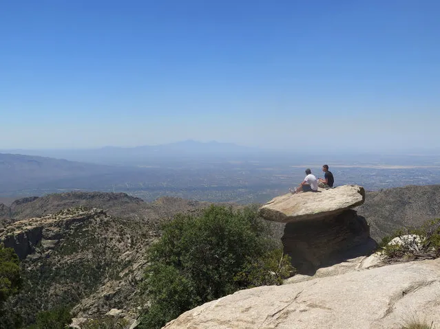 In this Friday, June 3, 2016 photo at Mount Lemmon, just north of Tucson, Ariz., students sit on a large rock overlooking the landscape. Many in Tucson escape to Mount Lemmon as temperatures rise to triple-digits, heading warnings of excessive heat. Mount Lemmon is the highest point in the Santa Catalina Mountains and offers temperatures that are on average 20 degrees cooler than the city. (Photo by Astrid Galvan/AP Photo)