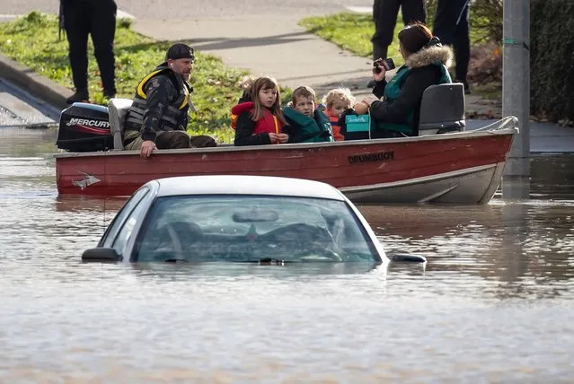 A woman and children who were stranded by high water due to flooding are rescued by a volunteer operating a boat as another person's car is submerged near them in Abbotsford, British Columbia, on Tuesday, November 16, 2021. (Photo by Darryl Dyck/The Canadian Press via AP Photo)