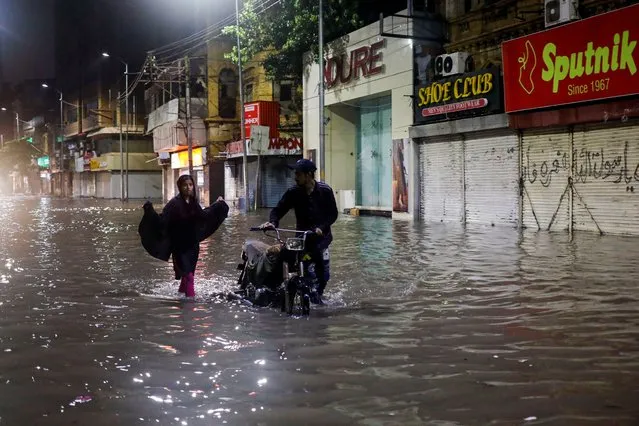 A couple with their motorcycle walk through a flooded business street following heavy rains during the monsoon season in Karachi, Pakistan on July 24, 2022. (Photo by Akhtar Soomro/Reuters)