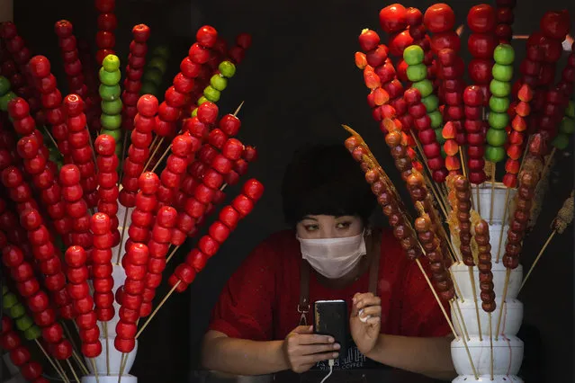 A vendor wearing a protective face mask looks out of her store selling sugar-coated haws on a stick in Beijing, Sunday, April 12, 2020. (Photo by Andy Wong/AP Photo)