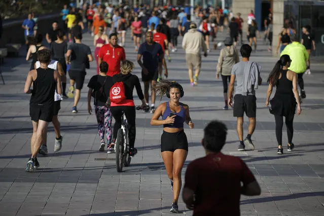 People exercise on a seafront promenade in this photo taken with a telephoto lens in Barcelona, Spain, Saturday, May 2, 2020. Spaniards have filled the streets of the country to do exercise for the first time after seven weeks of confinement in their homes to fight the coronavirus pandemic. People ran, walked, or rode bicycles under a brilliant sunny sky in Barcelona on Saturday, where many flocked to the maritime promenade to get as close as possible to the still off-limits beach. (Photo by Emilio Morenatti/AP Photo)