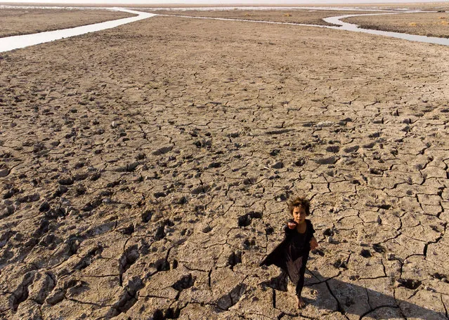 A child walks on the dried-up bed of Iraq's receding southern marshes of Chibayish in Dhi Qar province on August 23, 2022. (Photo by Hussein Faleh/AFP Photo)