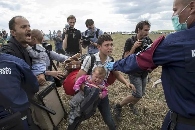 A migrant carrying a baby is stopped by a Hungarian policeman as he tries to escape a collection point in Roszke village, Hungary, September 8, 2015. (Photo by Marko Djurica/Reuters)