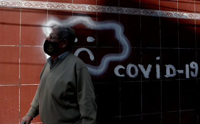 A man wearing a mask to curb the spread of the new coronavirus walks past COVID-19 graffiti, in La Paz, Bolivia, Wednesday, June 24, 2020. (Photo by Juan Karita/AP Photo)