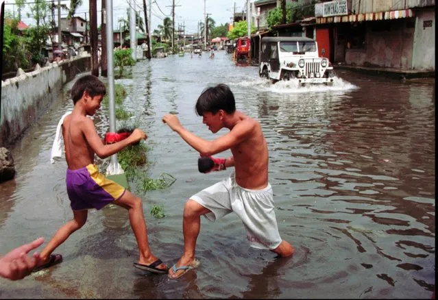 Two boys playfully slug it out with one boxing glove each Wednesday September 18, 1996 along a flooded street at northern Manila suburb of Kalookan following heavy rains overnight. Boxing is slowly becoming popular here following the silver medal finish of a Filipino light flyweight boxer in the Atlanta Olympics. (Photo by Alberto Marquez/AP Photo)