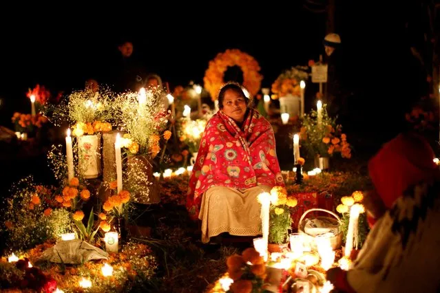 A woman sits next to a grave during the Day of the Dead at a cemetery in the Purepecha indigenous community of Cucuchuchu, Michoacan state, Mexico on November 2, 2022. (Photo by Raquel Cunha/Reuters)