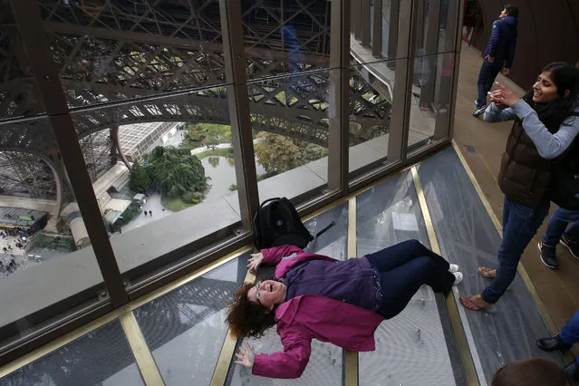 A Visitors takes a photo on the new glass floor at The Eiffel Tower, during the inauguration of the newly refurbish first floor, in Paris, France, Monday, October 6, 2014. Visitors of the Eiffel Tower can walk on a transparent floor at 188 feet high and look down through solid glass, with safety glass barriers around the edge. (Photo by Francois Mori/AP Photo)