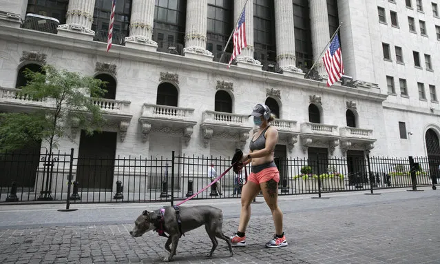 A woman wearing a mask walks her dog past the New York Stock Exchange, Tuesday, June 30, 2020, during the coronavirus pandemic. (Photo by Mark Lennihan/AP Photo)