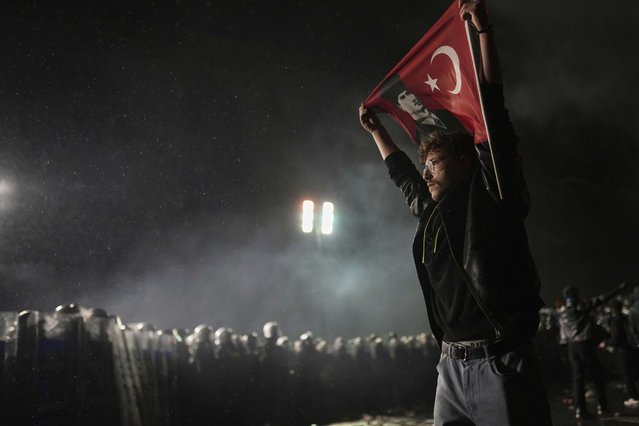 A protester holds a Turkish flag as riot police stand guard during a protest after Istanbul's Mayor Ekrem Imamoglu was arrested and sent to prison, in Istanbul, Turkey, Sunday, March 23, 2025. (Photo by Francisco Seco/AP Photo)
