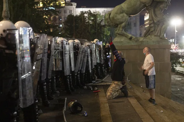 A protester kneels in front of riot police on the steps of the Serbian parliament in Belgrade, Serbia, Friday, July 10, 2020. (Photo by Marko Drobnjakovic/AP Photo)