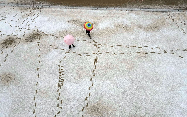 Two students holding umbrellas leave their footprints on a snow-covered playground amid a heavy snow advisory at Yongnam Elementary School in the southeastern city of Changwon, South Korea, 12 February 2025. (Photo by Yonhap/EPA)
