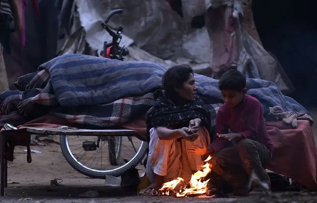 An Indian woman sits next to a fire with her son on a cold winter morning on the outskirts of New Delhi on January 3, 2018. (Photo by Prakash Singh/AFP Photo)