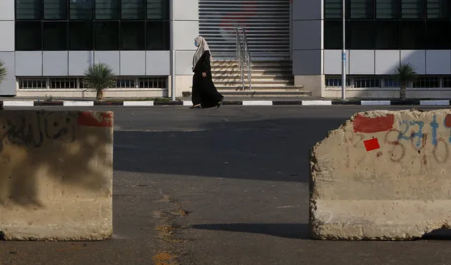 A Palestinian woman walks on a road next to barriers during a lockdown imposed following the discovery of a rise in coronavirus cases in Gaza City, Monday, August 31, 2020. (Photo by Hatem Moussa/AP Photo)