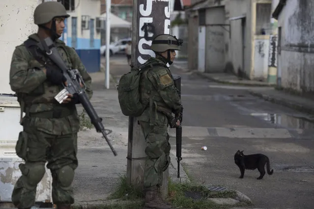 A cat stands next to Brazilian marines patrolling, during surprise operation in Kelson's slum in Rio de Janeiro, Brazil, Tuesday, February 20, 2018. Members of the armed forces and the police spread out in the slum in northern Rio in the first major operation since the military took control of security forces in the state. (Photo by Leo Correa/AP Photo)