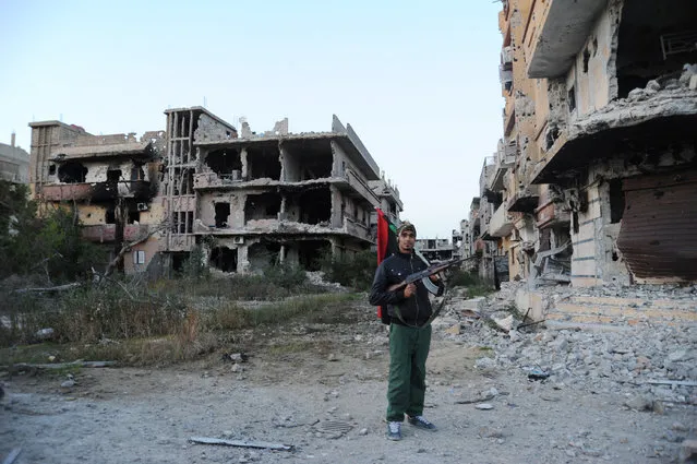 In this February 23, 2016 file photo, a civilian fighter holding the Libyan flag stands in front of damaged buildings in Benghazi, Libya. Amnesty International, an international rights group expressed alarm Friday, September 30, 2016, over the fate of hundreds of Libyan and foreign nationals trapped for months amid fighting in the eastern city of Benghazi. Amnesty International said that nearly 130 families and hundreds of foreigners in the southwestern Benghazi neighborhood of Ganfouda have been cut off from the outside world, with dwindling food and fuel supplies. (Photo by Mohammed el-Shaiky/AP Photo)