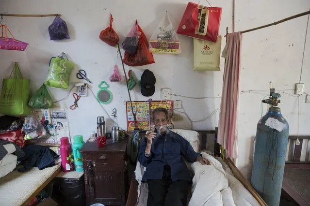 Wang Tianfang, a 87 year old pneumoconiosis patient smokes next to an oxygen supply, which he needs several hours per-day, in his room at Yangjia Hospital in Wuyi County, Zhejiang Province, China October 19, 2015. Tianfang, a former miner, was diagnosed with dust lung in 1973 and has lived at Yangjia Hospital for two years. (Photo by Damir Sagolj/Reuters)