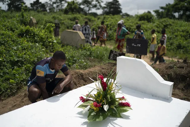 A man prays over the grave of a relative after painting the gravestone white, as a symbol that the soul of the deceased remains in peace, as members of the family stand by, during the Day of the Dead celebrations in Abidjan, Ivory Coast, Monday, November 2, 2020. (Photo by Leo Correa/AP Photo)