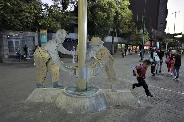 A boy jumps near the “Los Petroleros” sculpture that shows two men working on an oil drill of Petroleos de Venezuela, S.A, PDVSA, on the Sabana Grande boulevard, in Caracas, Venezuela, March 20, 2023. Venezuela's oil czar, Tareck El Aissami announced his resignation on Twitter and pledged to help investigate any allegations involving PDVSA. (Photo by Ariana Cubillos/AP Photo)