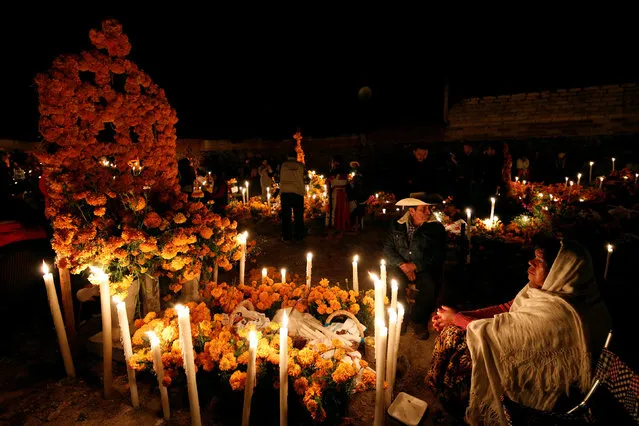 A couple gather next to the tomb of their loved one on the Day of the Dead, at a cemetery in Arocutin, in Michoacan state, Mexico November 1, 2016. (Photo by Alan Ortega/Reuters)