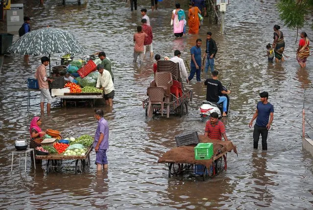 People buy vegetables from street vendors as others wade through a waterlogged road after heavy rains in Ahmedabad, India on June 26, 2023. (Photo by Amit Dave/Reuters)