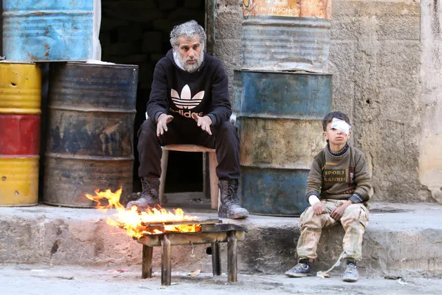 An injured boy sits near a man as they warm themselves by a fire in a rebel held area of Aleppo, Syria November 18, 2016. (Photo by Abdalrhman Ismail/Reuters)