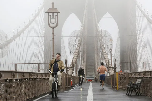 Bicyclists and a jogger cross the Brooklyn Bridge in a heavy fog, Wednesday, December 23, 2015 in New York.  (Photo by Mark Lennihan/AP Photo)