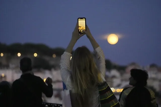 A woman takes pictures of a supermoon rising above Lisbon, Wednesday, August 30, 2023. It's the month's second supermoon, when a full moon appears a little bigger and brighter thanks to its slightly closer position to Earth. (Photo by Armando Franca/AP Photo)