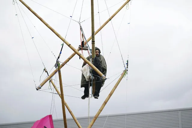 An Animal Rebellion protester suspended from a bamboo structure outside a McDonald's distribution site in Hemel Hempstead, England, Saturday May 22, 2021. (Photo by Yui Mok/PA Wire via AP Photo)