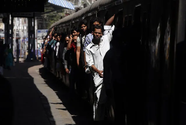 Local commuters hang out of an overcrowded suburban train as it arrives in Mumbai Central Train Station in Mumbai, India, Friday, January 22, 2016. Over 7.5 million people commute daily in the Mumbai suburban service which runs nearly 3,000 trips a day. (Photo by Rajanish Kakade/AP Photo)