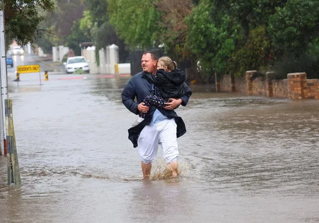 A man carries a child as he wades trough a flooded road following heavy rains in Strand, Western Cape, South Africa on September 25, 2023. (Photo by Esa Alexander/Reuters)